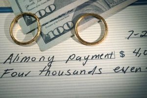 two wedding bands on top off two hundred dollar bills and a check that says alimony payment symbolizing Chicago alimony and spousal support payments 